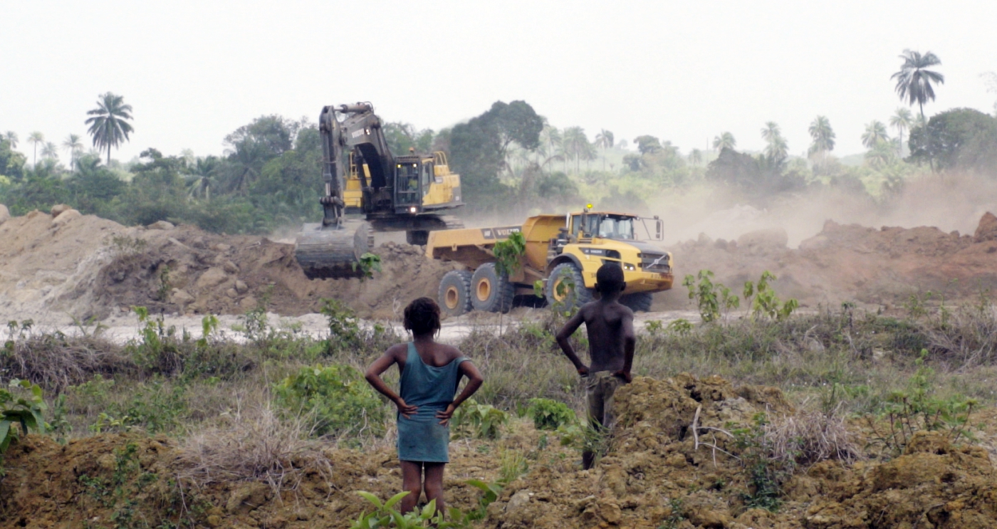 Two children watch as tractors from Sierra Rutile Ltd. dig up the land.
