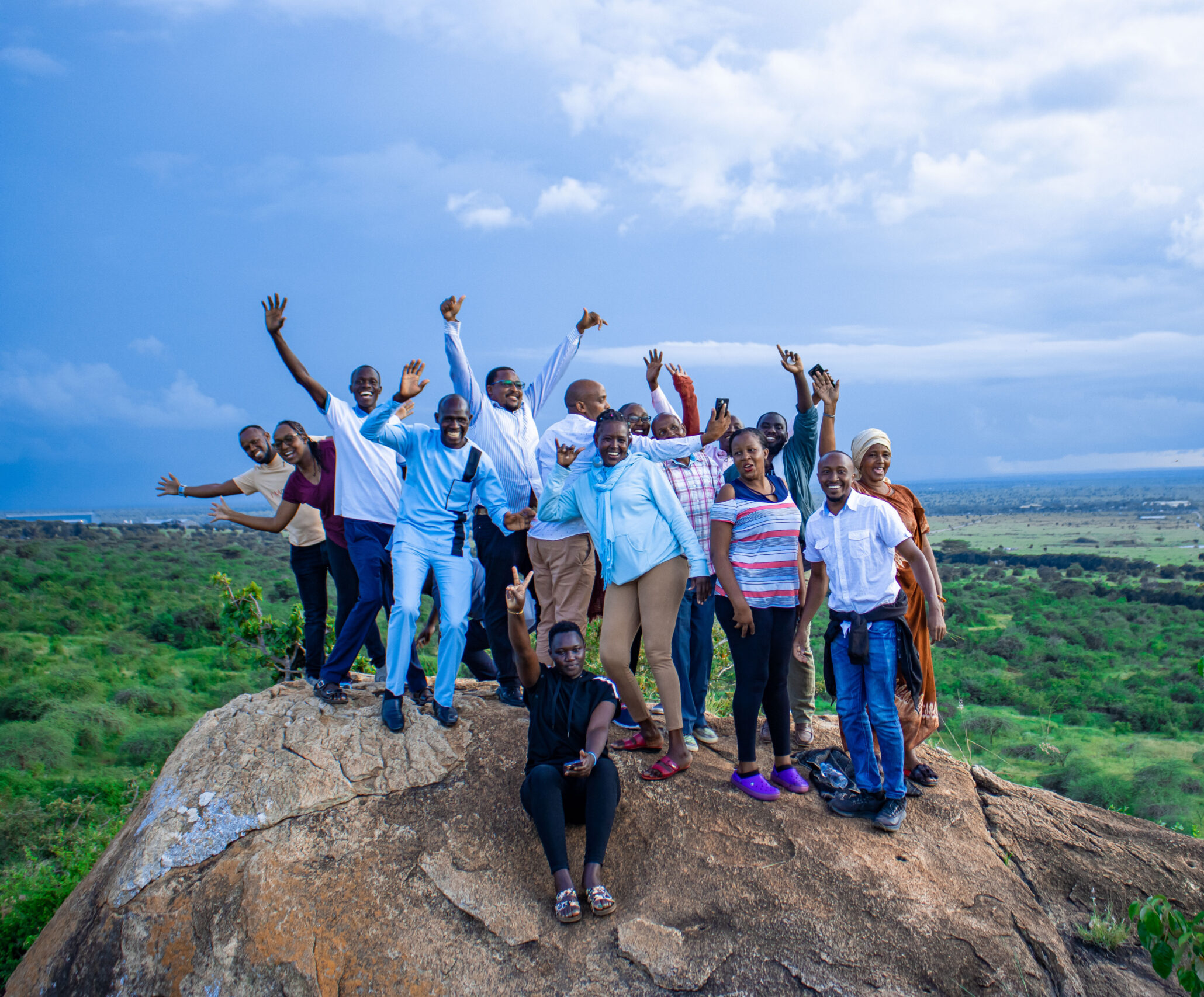 A group of people pose atop a rocky outcropping under a cloudy but blue sky.
